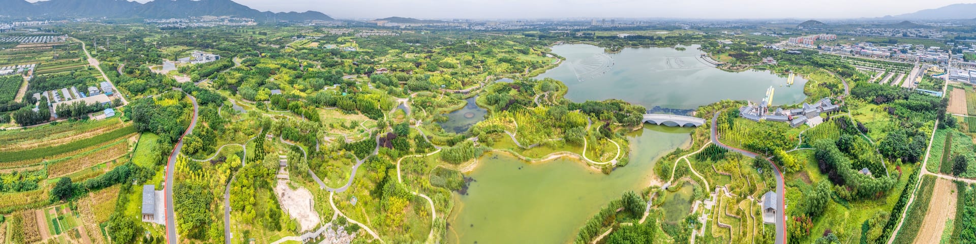 A panoramic view of a city with a large lake, green parks, and distant mountains.