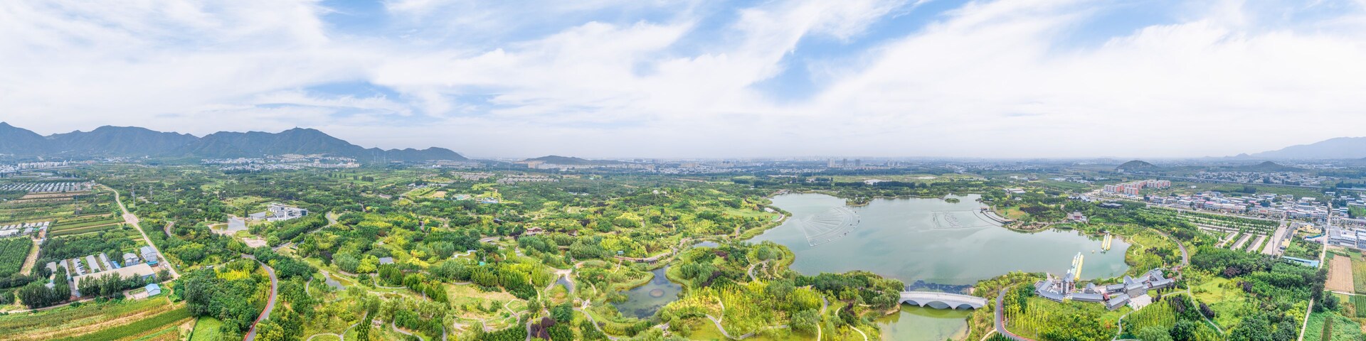 Vista panorâmica de uma cidade com um grande lago, parques verdes e montanhas ao longe.