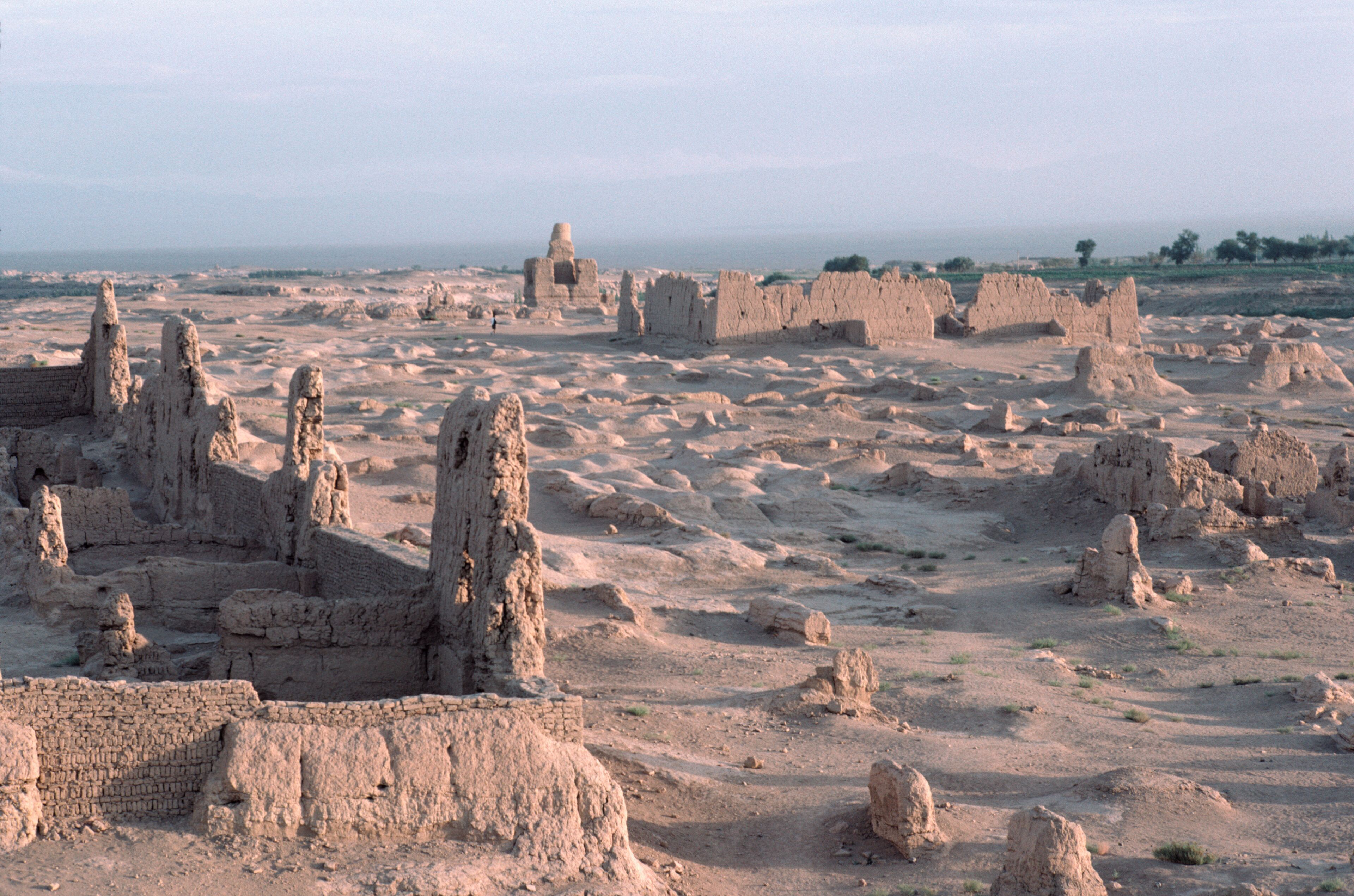 Ancient ruins with multiple stone structures and a distant view of the sea.