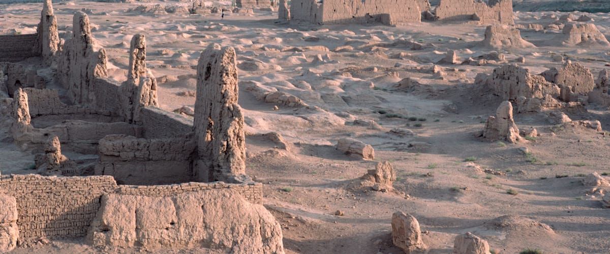 Ancient ruins with multiple stone structures and a distant view of the sea.