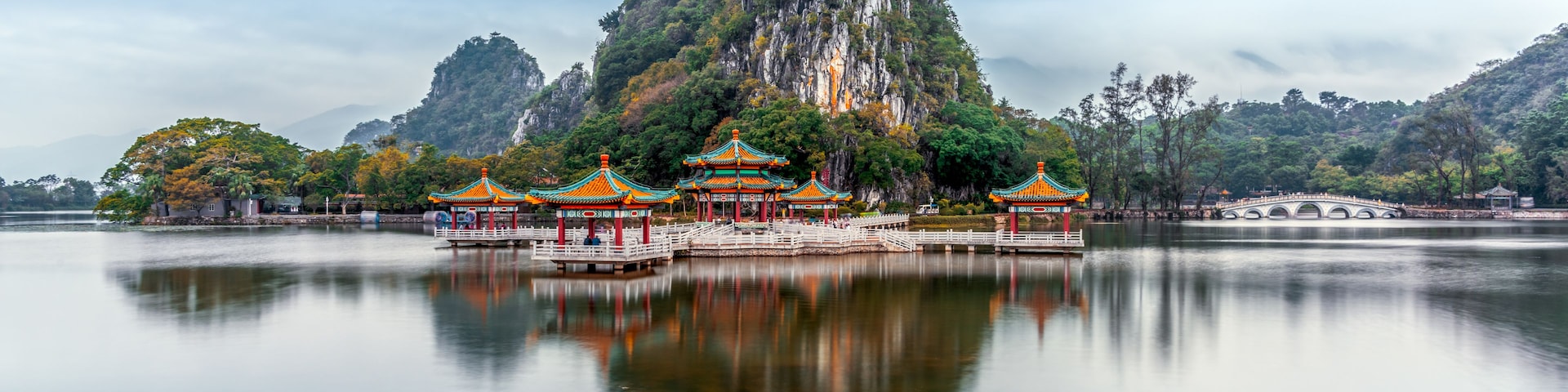 Um complexo de templos chineses tradicional, com várias pagodes, uma montanha imponente e um lago tranquilo.