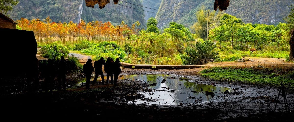 A cave entrance with a view of a forested valley and a waterfall.