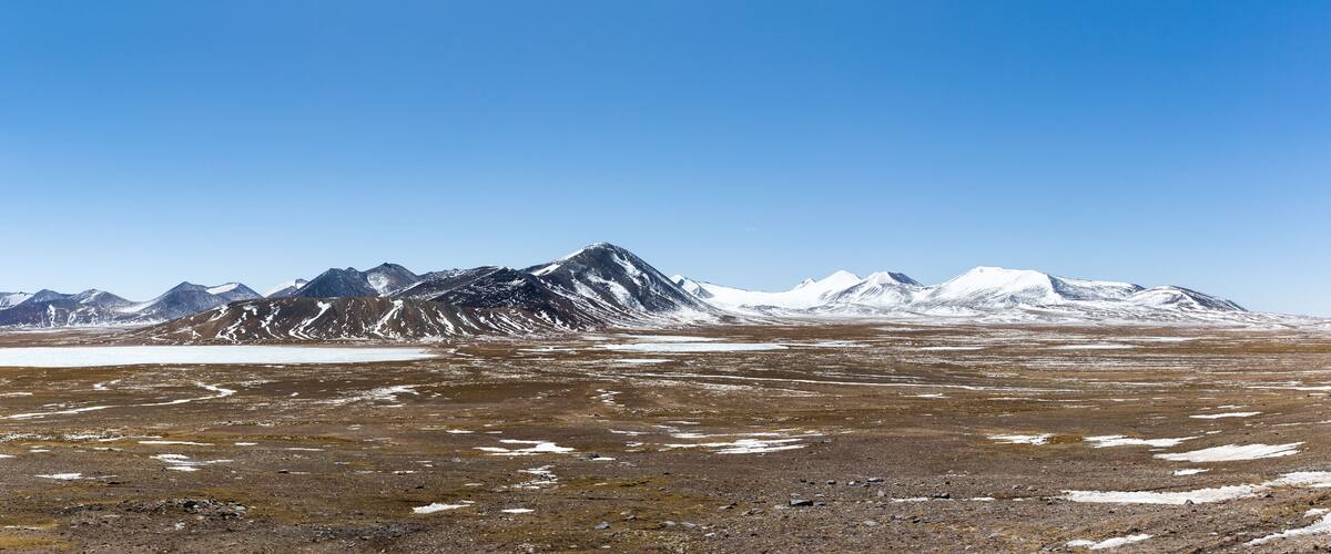 A mountainous landscape with snow-capped peaks and a barren terrain.