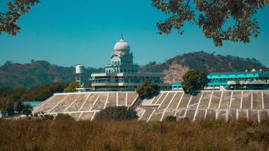 A large building with a dome, surrounded by dry grass and hills.