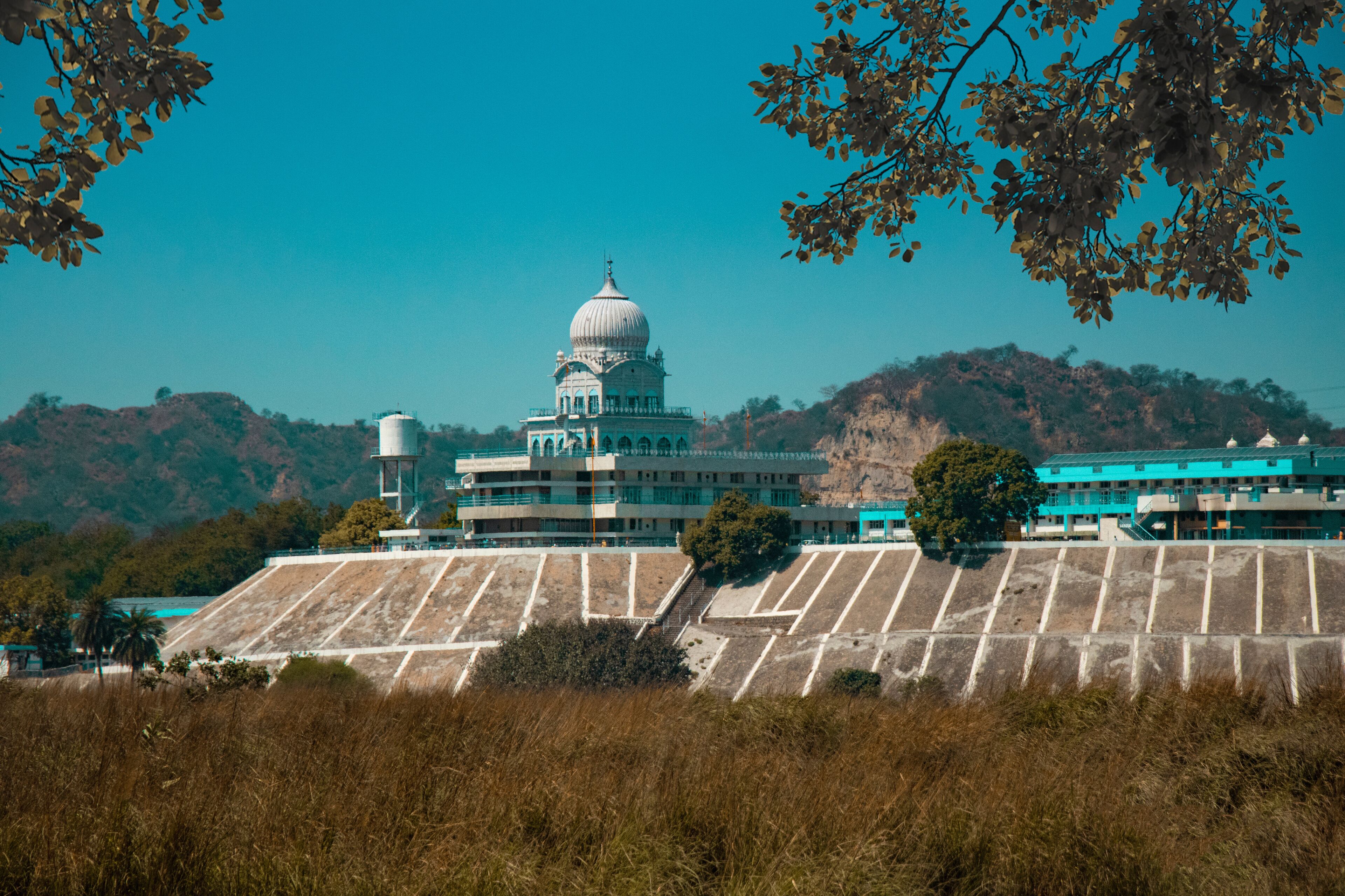 A large building with a dome, surrounded by dry grass and hills.