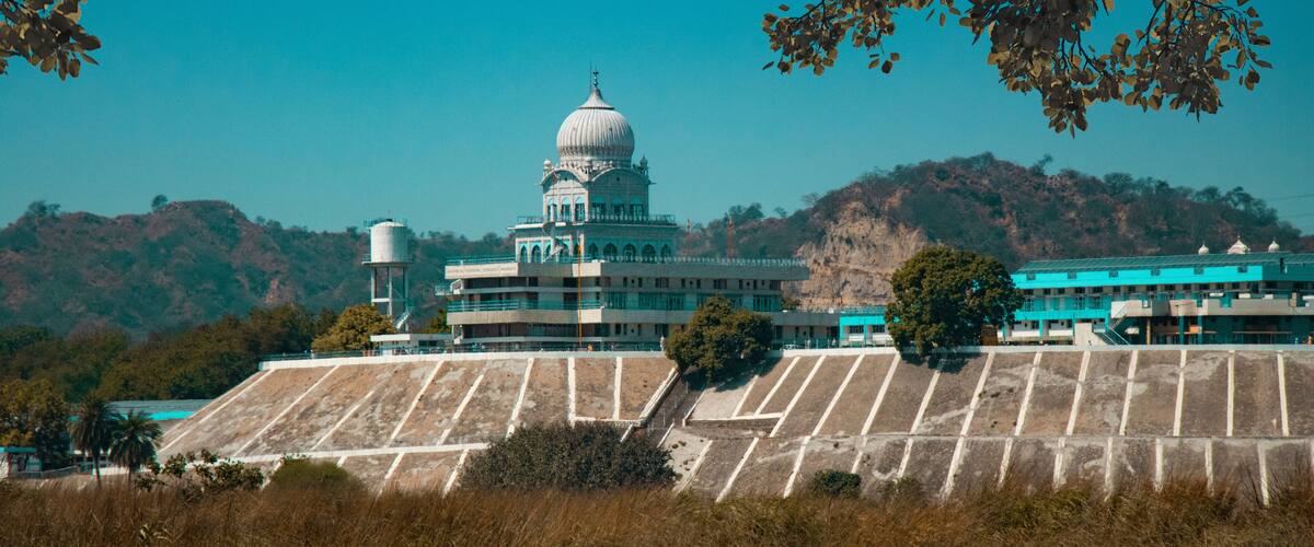 A large building with a dome, surrounded by dry grass and hills.