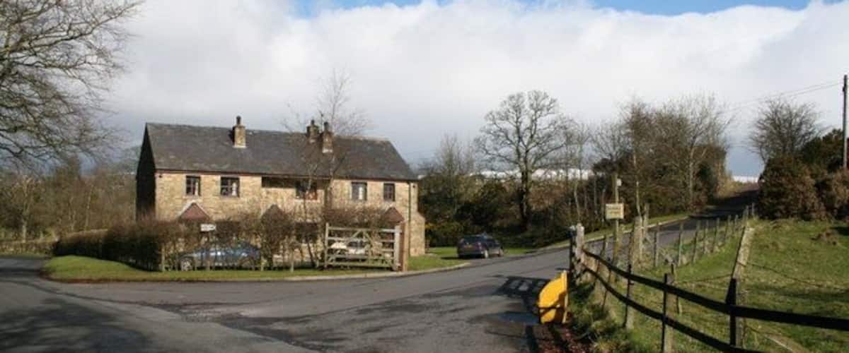A rural road with a stone house, a yellow post box, and a wooden fence.