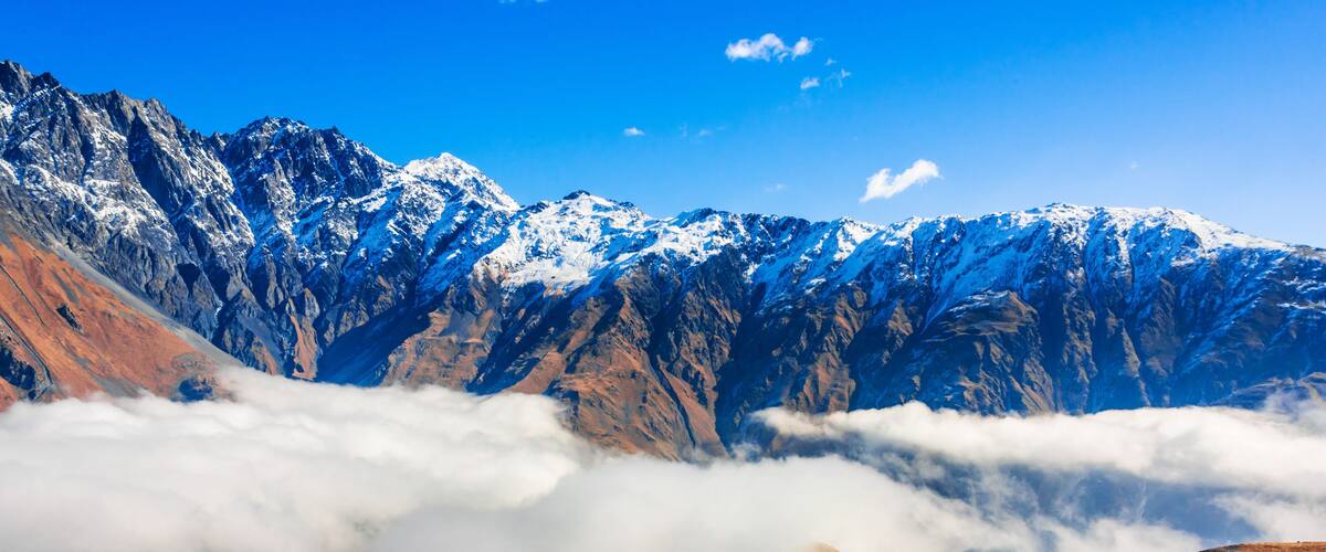 Snow-capped mountains, a valley with buildings, and a cloud-covered ridge.