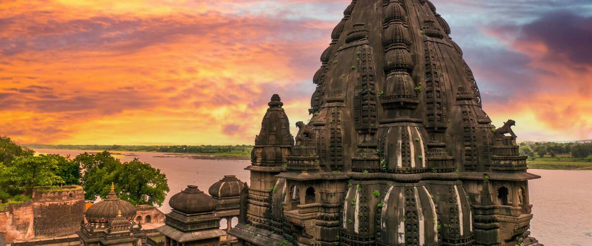 A temple with intricate architecture and a flag on top, set against a sunset sky.