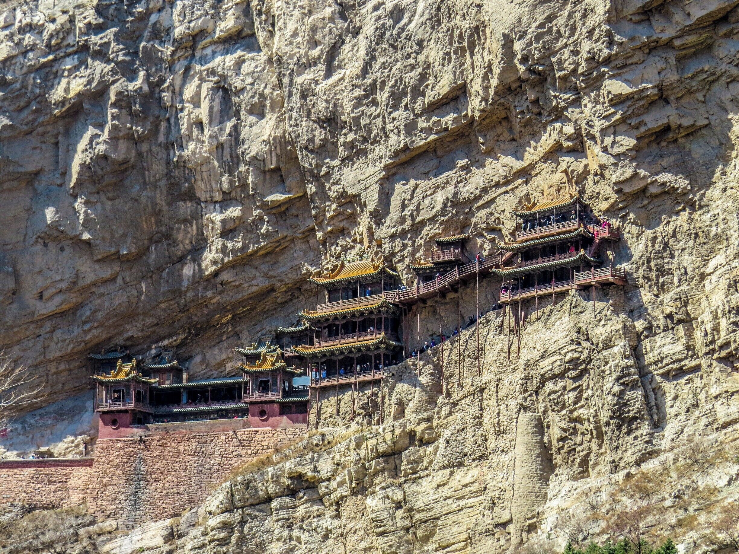 The Hanging Temple, built into a cliff (75 m or 246 ft above the ground) near Mount Heng in Hunyuan County, Datong, Shanxi province, China. Built more than 1,500 years ago, this temple is notable not only for its location on a sheer precipice but also because it is the only existing temple with the combination of three Chinese traditional religions: Buddhism, Taoism, and Confucianism. The structure is kept in place with oak crossbeams fitted into holes chiseled into the cliffs. The main supportive structure is hidden inside the bedrock. The monastery is located in the small canyon basin, and the body of the building hangs from the middle of the cliff under the prominent summit, protecting the temple from rain erosion and sunlight.