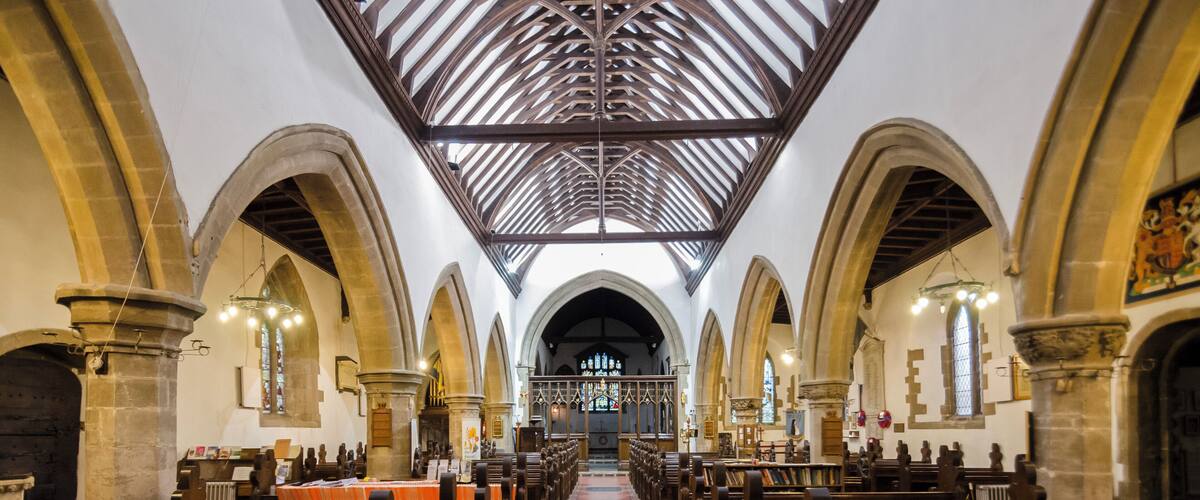 An interior of a church with wooden pews, arched ceilings, and stained glass windows.
