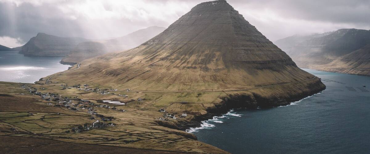 A coastal landscape with a prominent mountain, a small settlement, and a body of water.