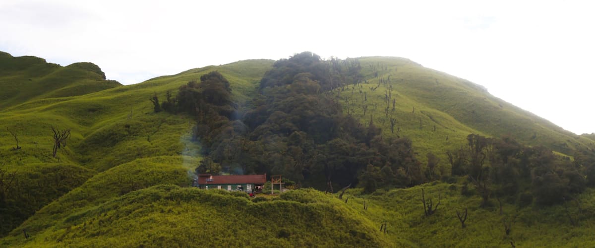 A house on a green hill with smoke rising from it.