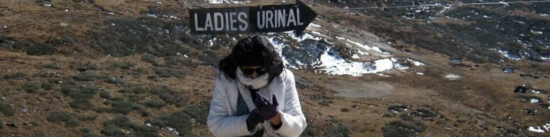 Una persona sentada sobre un saliente rocoso, con un letrero que dice “LADIES URINAL” al fondo.