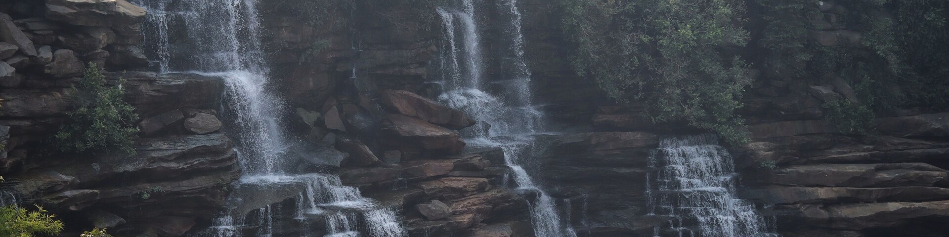 A multi-tiered waterfall cascading over rocky terrain with people observing from the top.