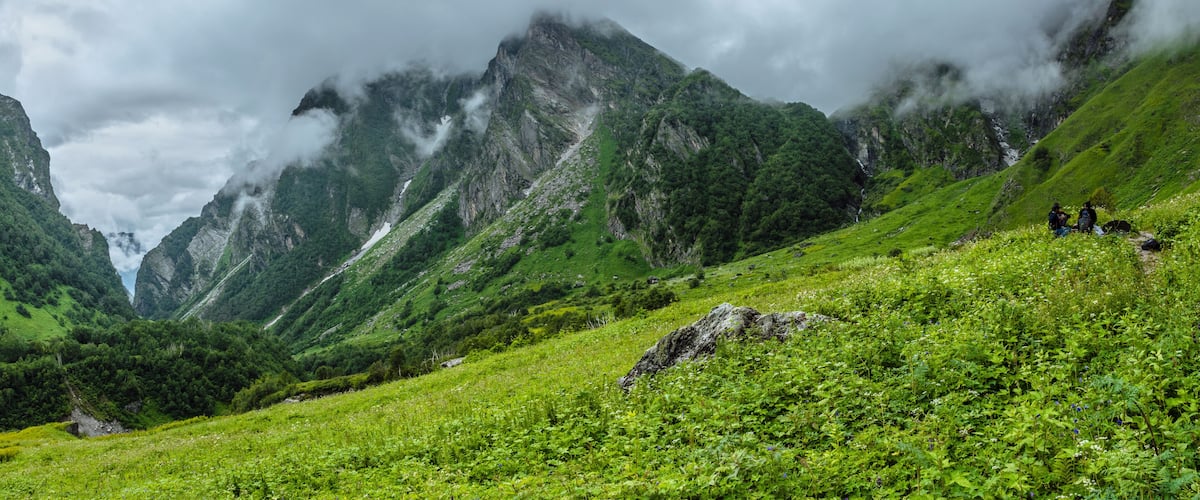 A mountainous landscape with lush green vegetation and hikers on a trail.