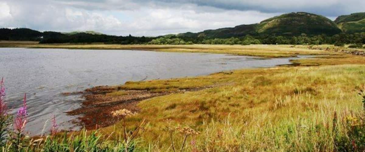 A lake with grassy banks and hills in the background.