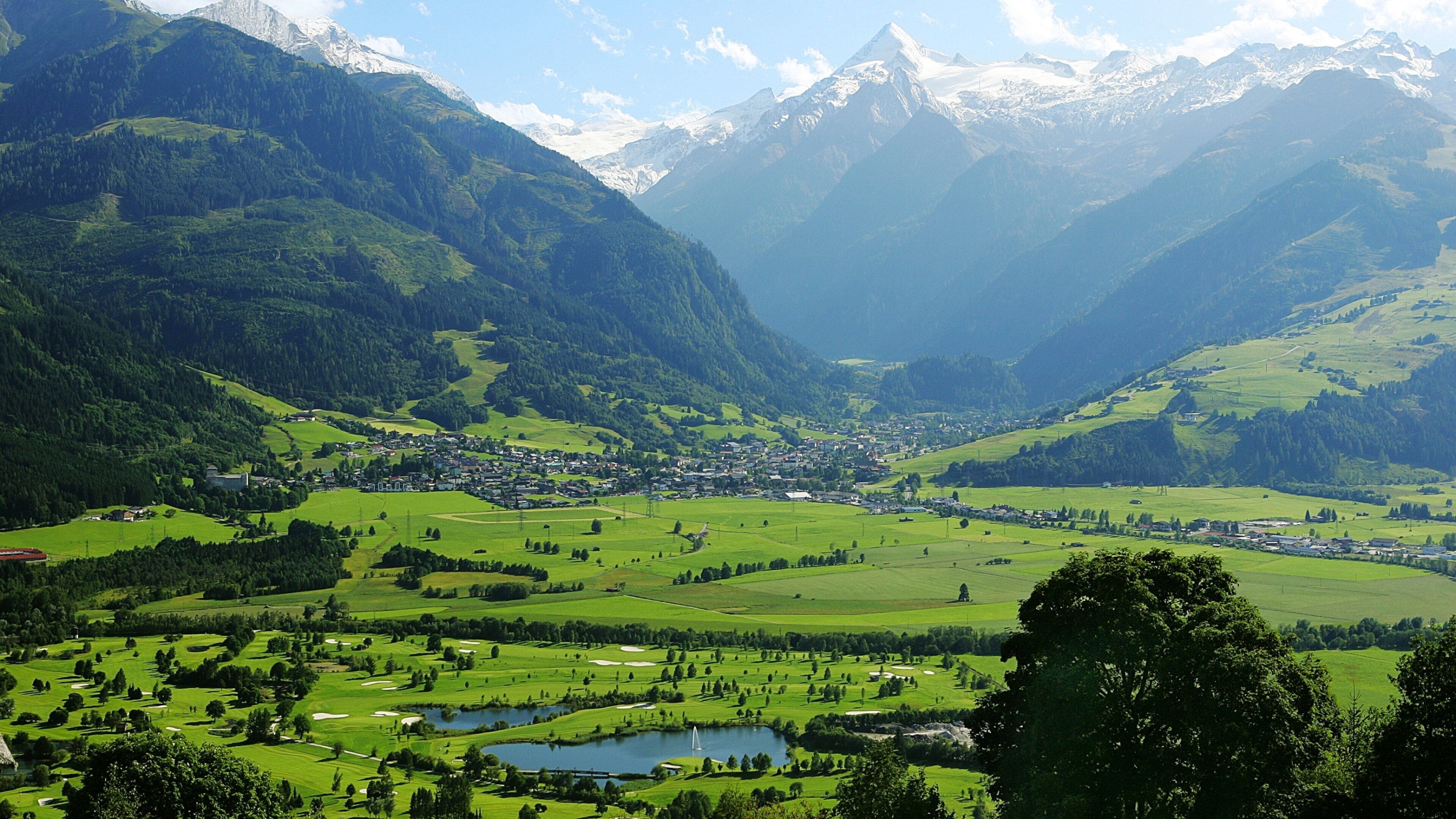 A valley with a town nestled between mountains, green fields, and a lake.