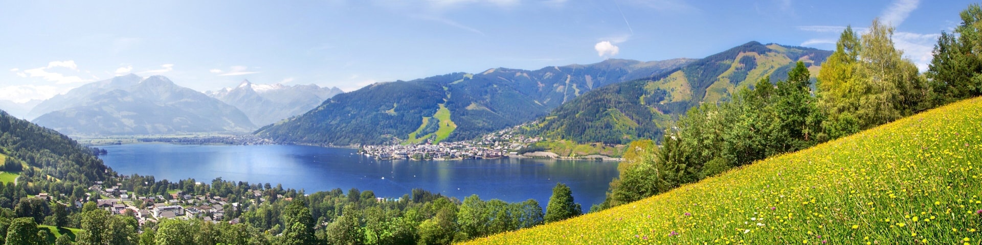 Ein See, umgeben von Bergen, einer Stadt und einem Feld voller gelber Blumen.