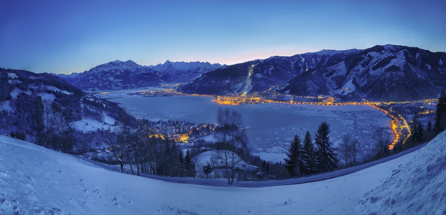 Un paisaje montañoso cubierto de nieve con un pueblo iluminado por luces a lo largo de un río.