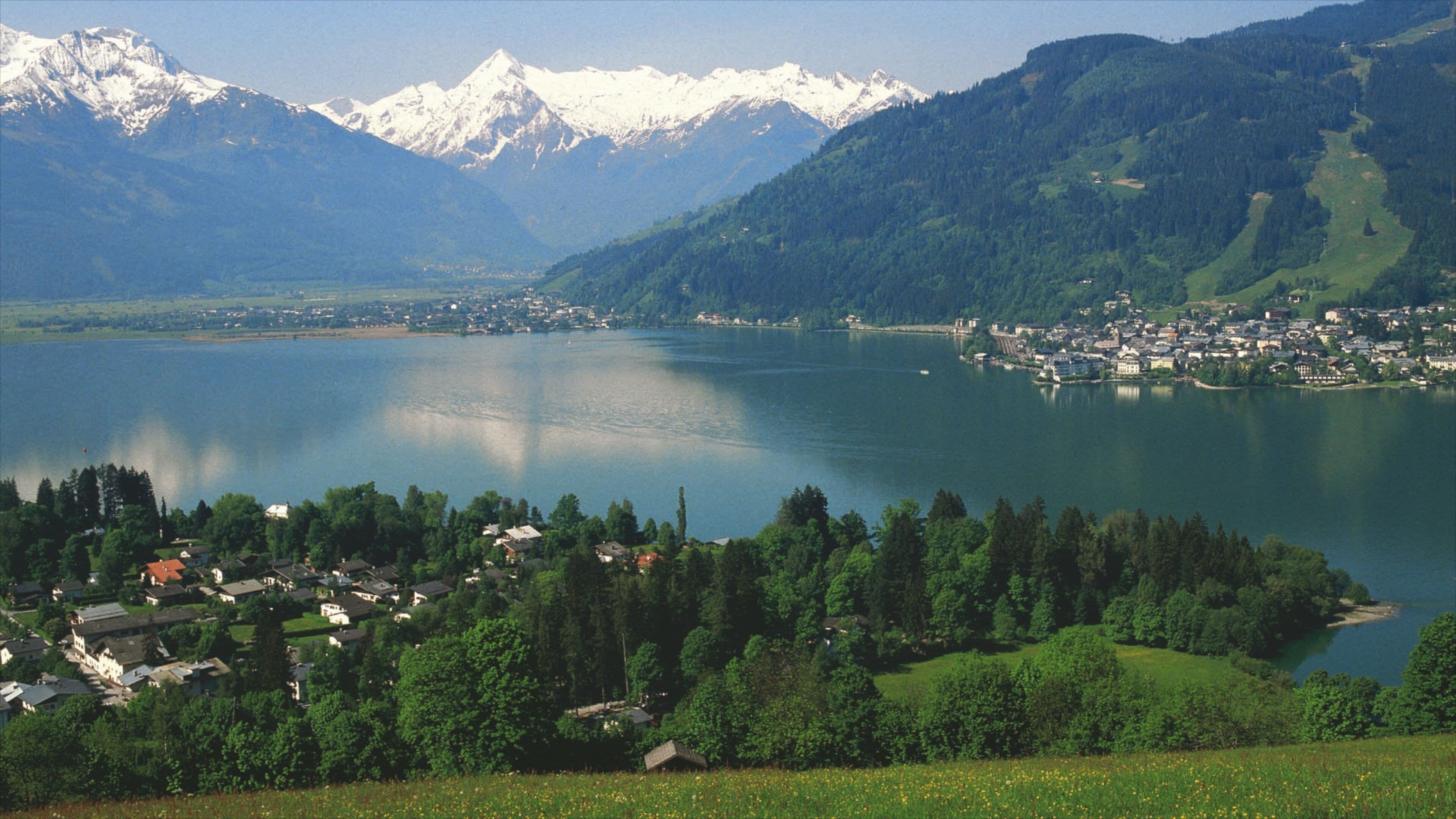 A lake surrounded by mountains and a small town with houses and trees.