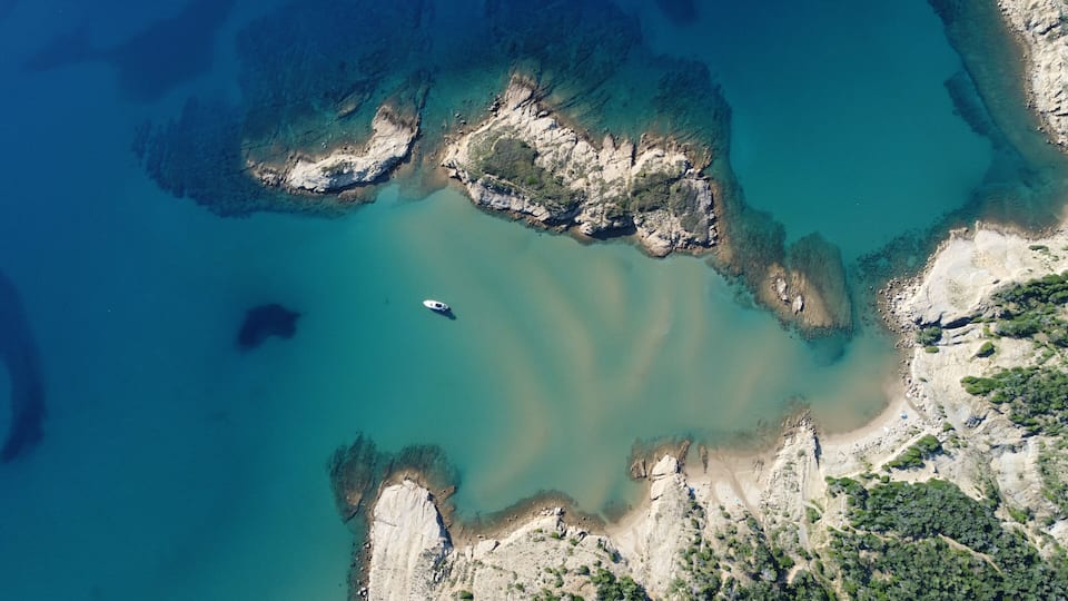 A coastal landscape with clear turquoise waters, rocky cliffs, and a small boat.