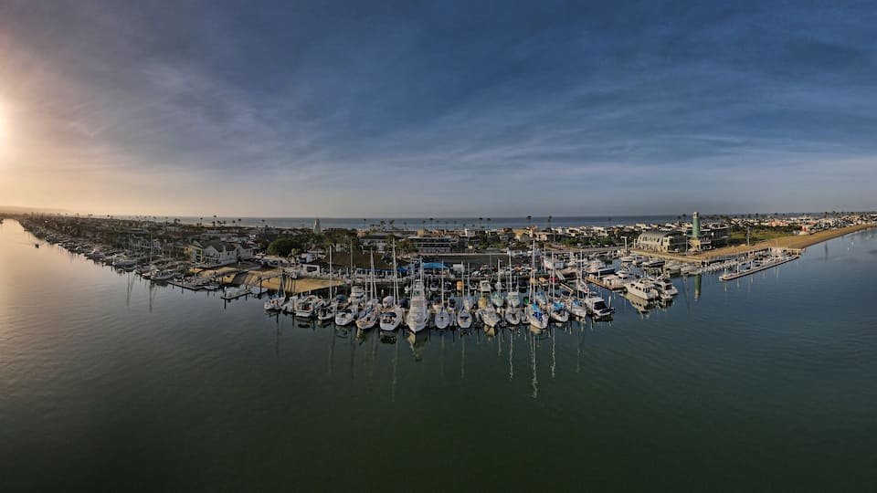 A marina with numerous boats docked, a bridge, and a lighthouse in the background.