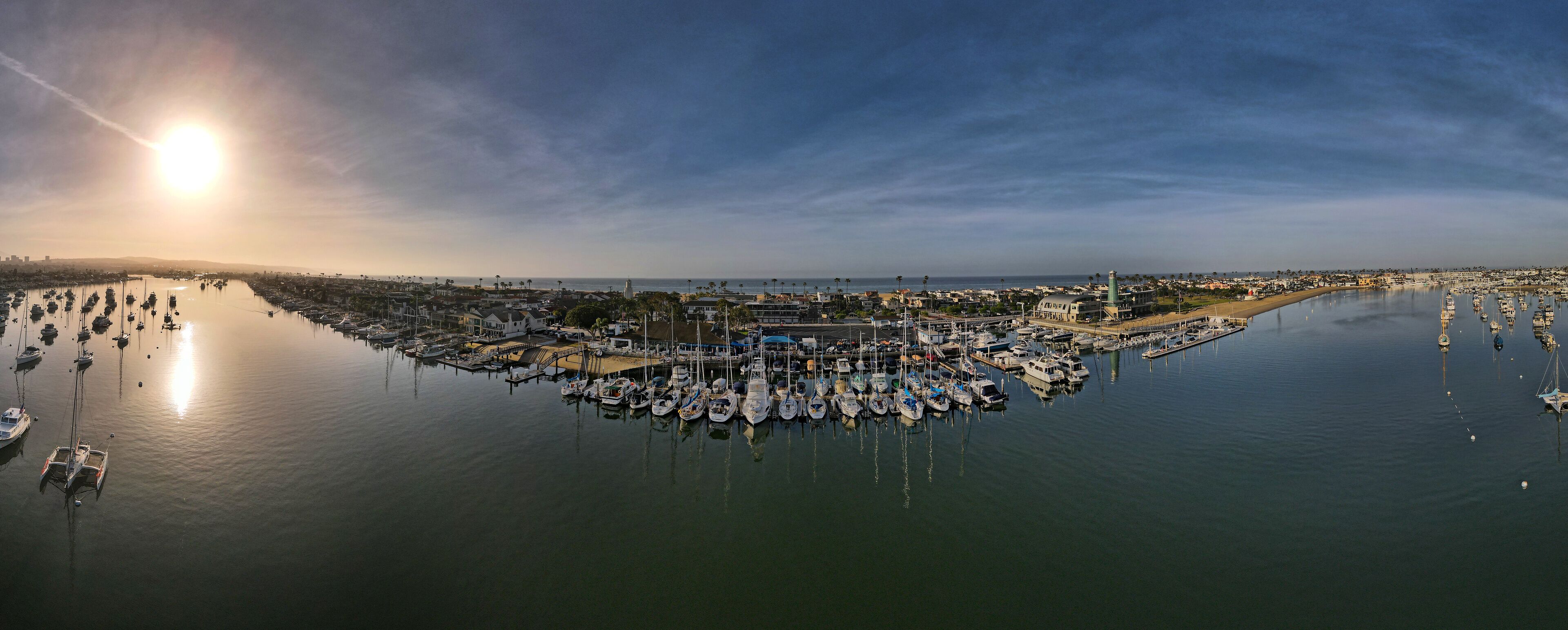 A marina with numerous boats docked, a bridge, and a lighthouse in the background.