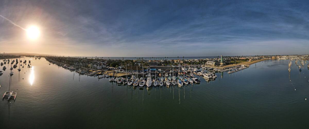 A marina with numerous boats docked, a bridge, and a lighthouse in the background.