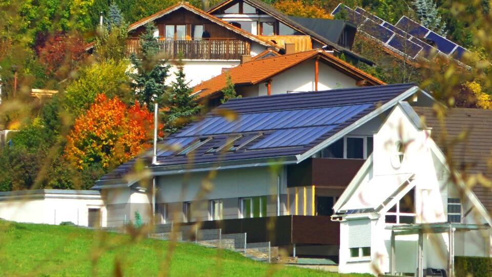A house with solar panels, surrounded by autumn trees and a grassy hill.