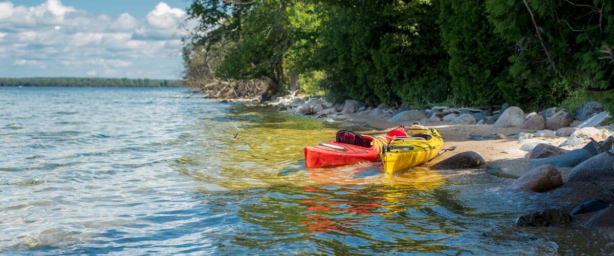 Kayaks on a calm riverbank with rocks and trees.