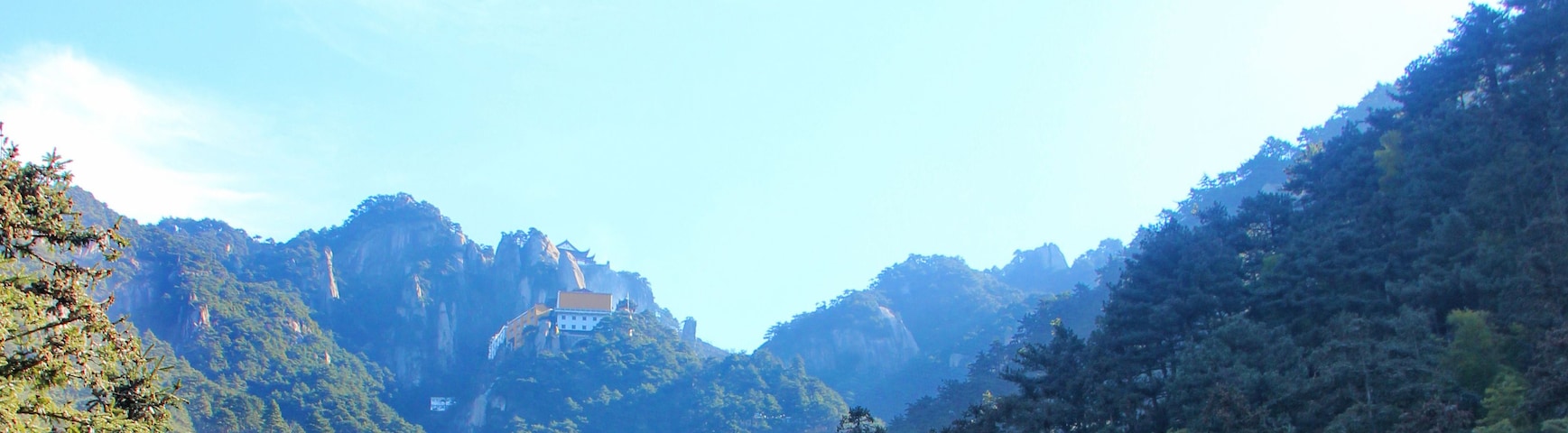 Un templo chino tradicional con una pagoda de varios niveles, rodeado de montañas verdes exuberantes y un cielo azul despejado.