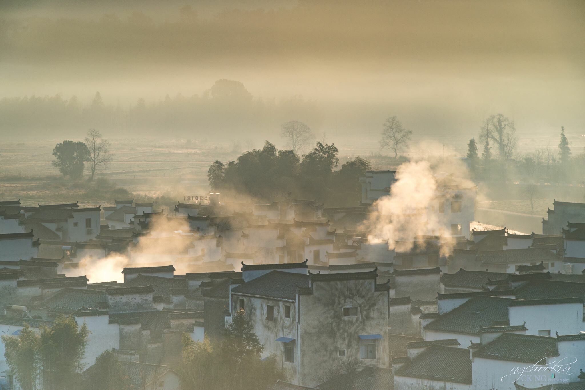 A misty village with traditional buildings and smoke rising from chimneys.
