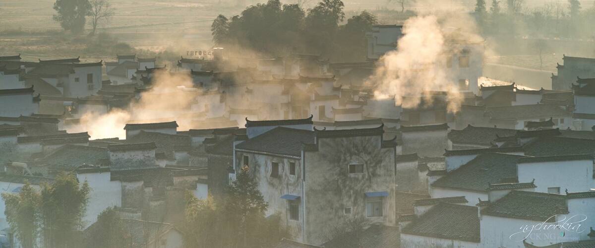 A misty village with traditional buildings and smoke rising from chimneys.