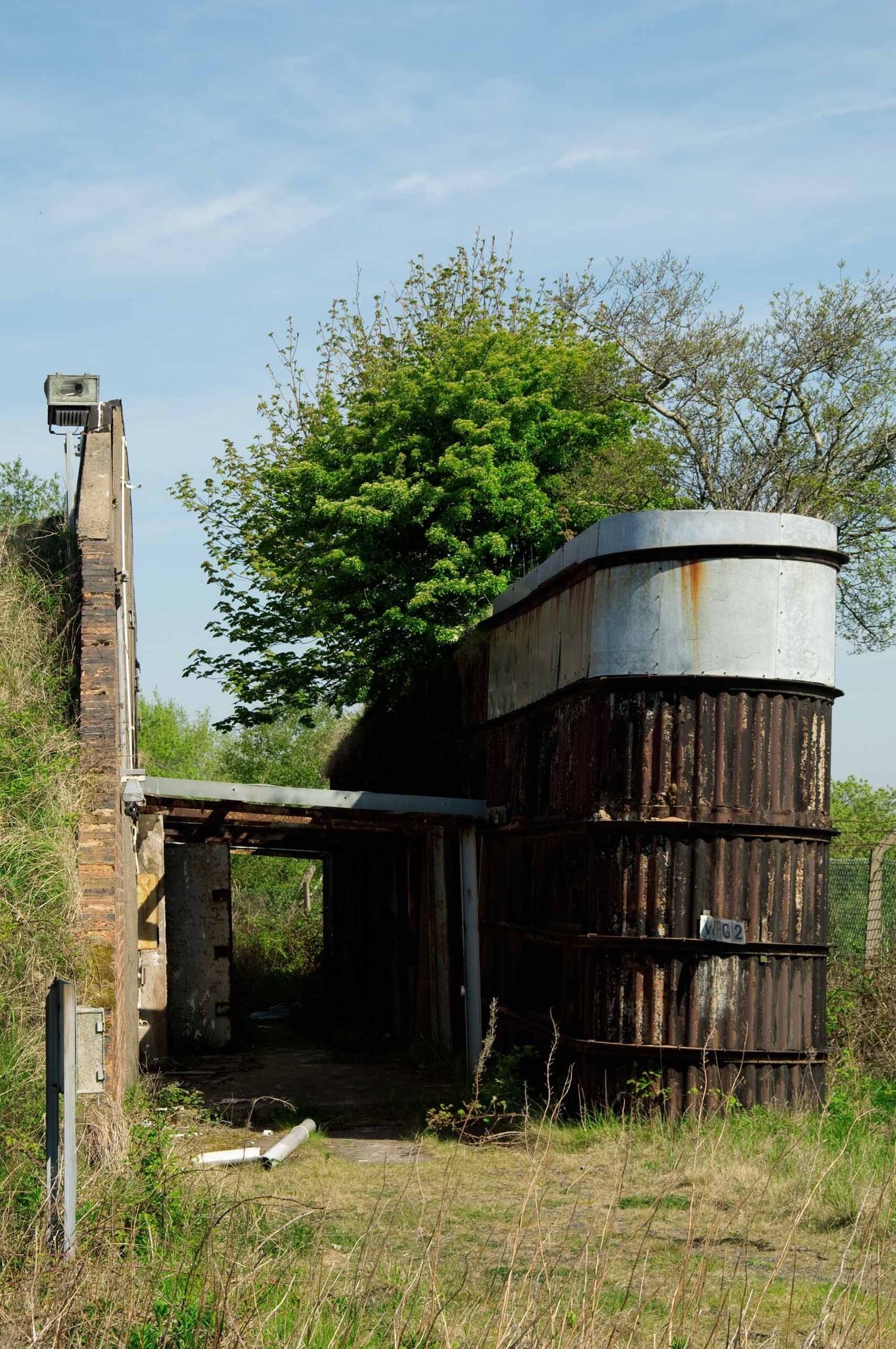 An abandoned industrial structure with rusted metal tanks and a brick chimney.