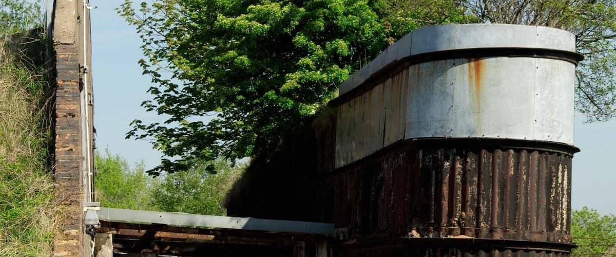 An abandoned industrial structure with rusted metal tanks and a brick chimney.