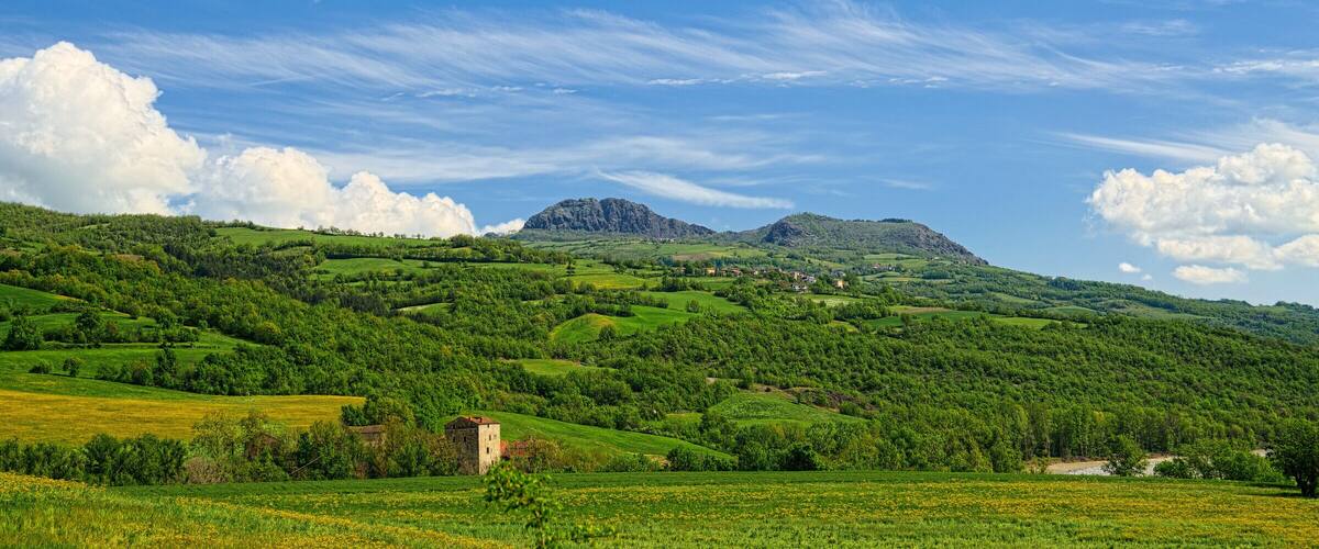 Rolling green hills, a small building, and a mountain in the distance under a blue sky with clouds.