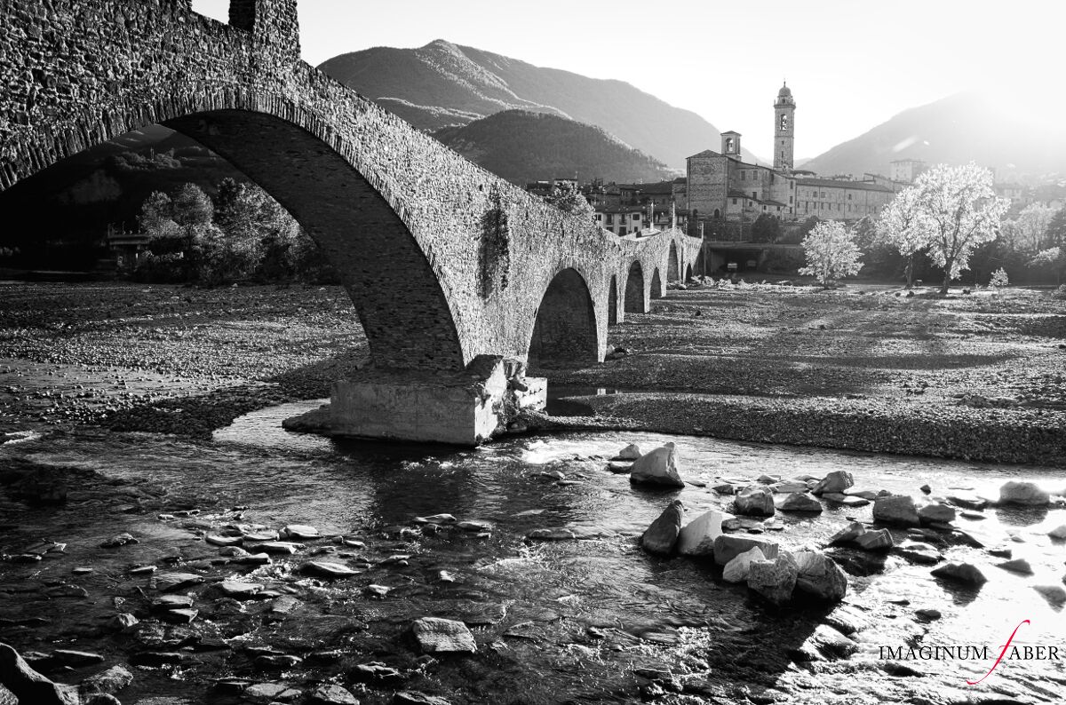 Bobbio is a small town in the province of Piacenza in Emilia-Romagna, northern Italy. It is located in the Trebbia River valley southwest of the town Piacenza, a valley described by Ernest Hemingway as "the most beautiful in the world". Depicted here is the Ponte Vecchio, called Ponte Gobbo (Hunchback Bridge), also known as the Devil's Bridge. It's an ancient stone bridge of Roman origin, which crosses the river Trebbia in eleven irregular arches.