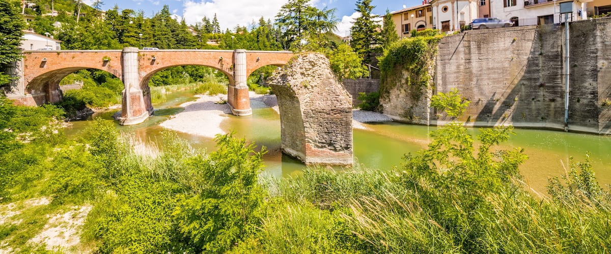 A stone bridge over a river, surrounded by greenery and buildings.