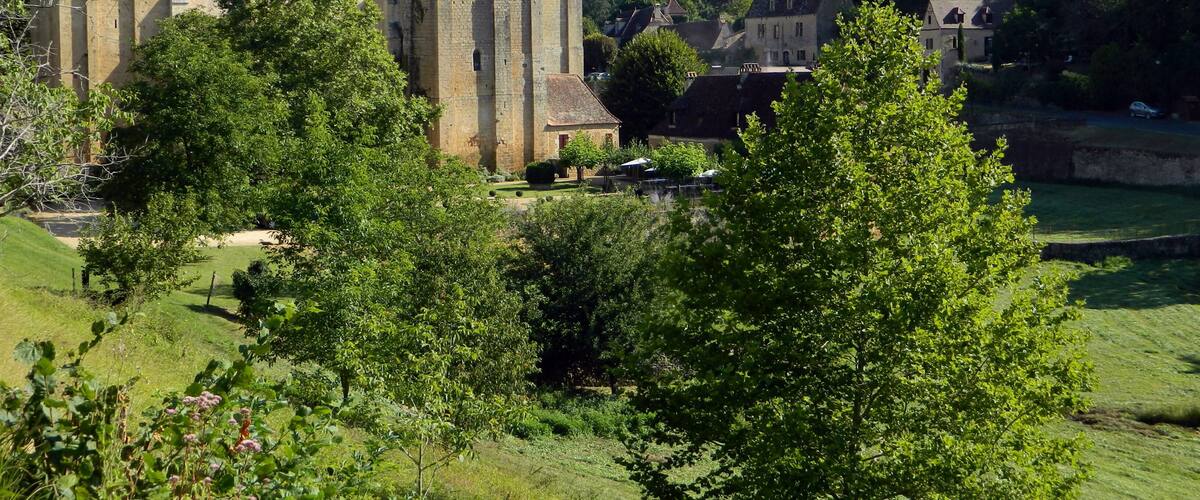 A historic stone church with a bell tower, surrounded by lush greenery and a small courtyard.