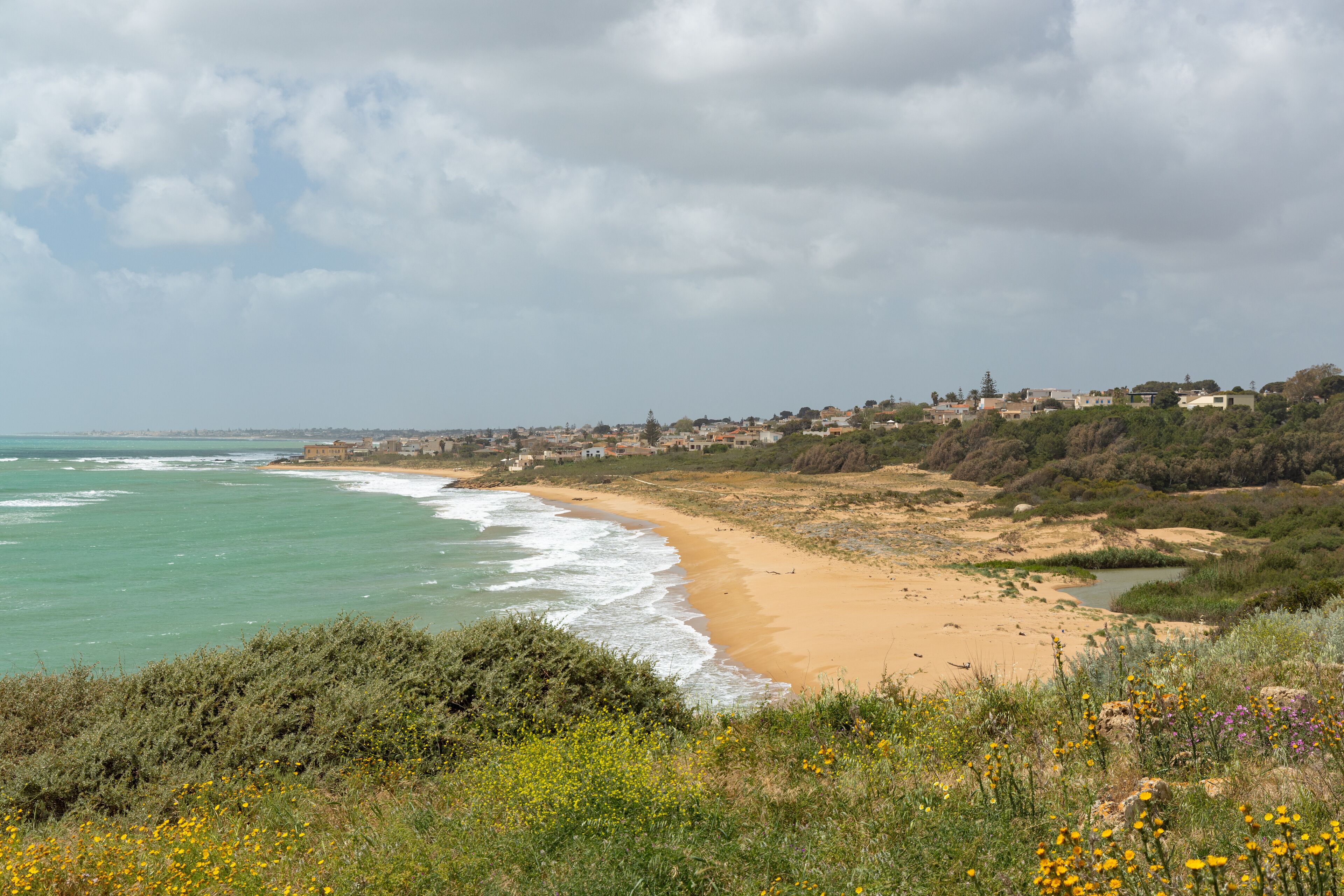 A coastal landscape with a sandy beach, ocean waves, and a town in the background.