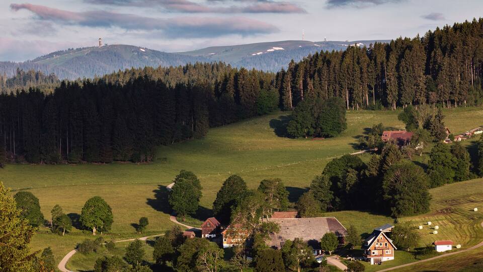 A rural landscape with a village, forested hills, and a clear sky.