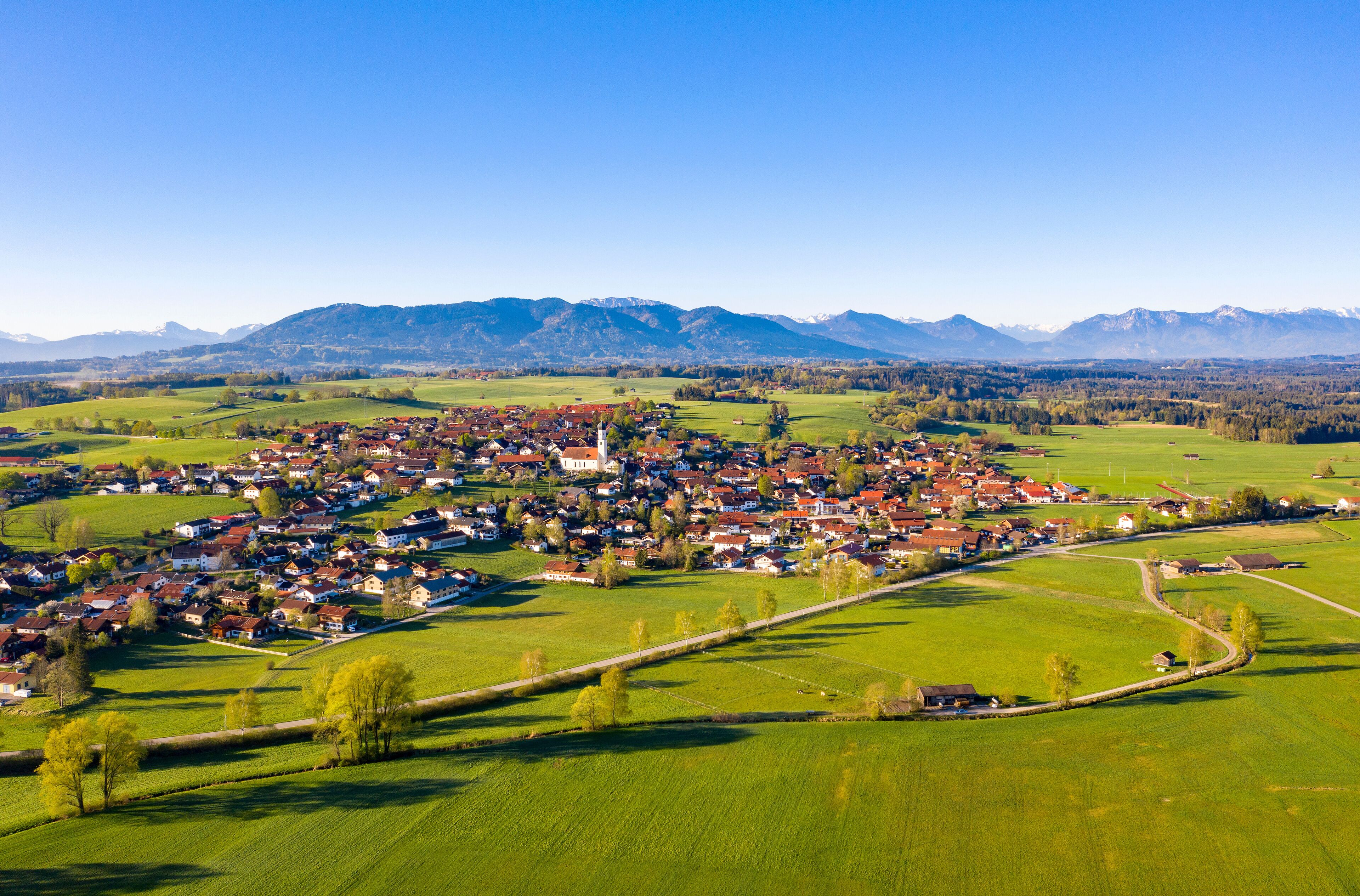 A village with red-roofed houses, a church, and mountains in the background.