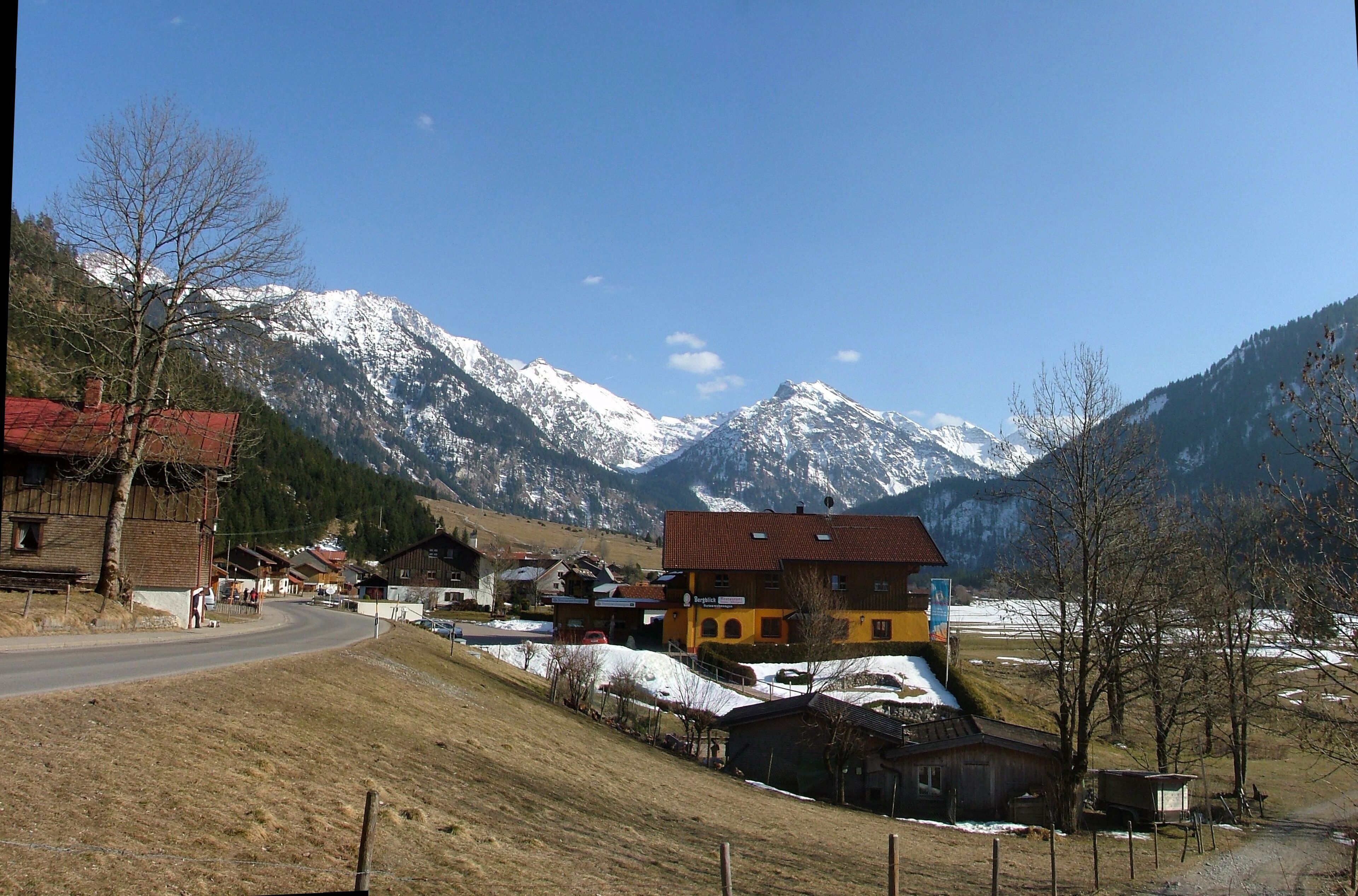 A mountain village with snow-capped peaks in the background, a winding road, and traditional houses.