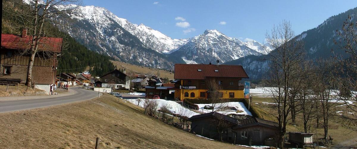 A mountain village with snow-capped peaks in the background, a winding road, and traditional houses.
