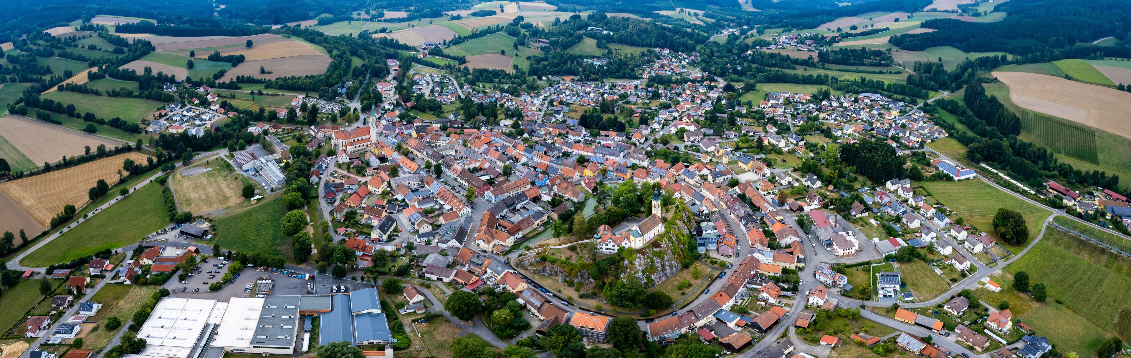 An aerial view of a town with a prominent church, surrounded by fields and residential areas.
