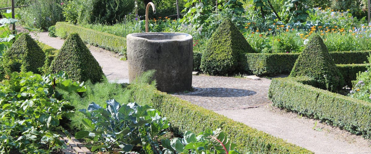 A garden with a central stone structure, neatly trimmed hedges, and a variety of plants.