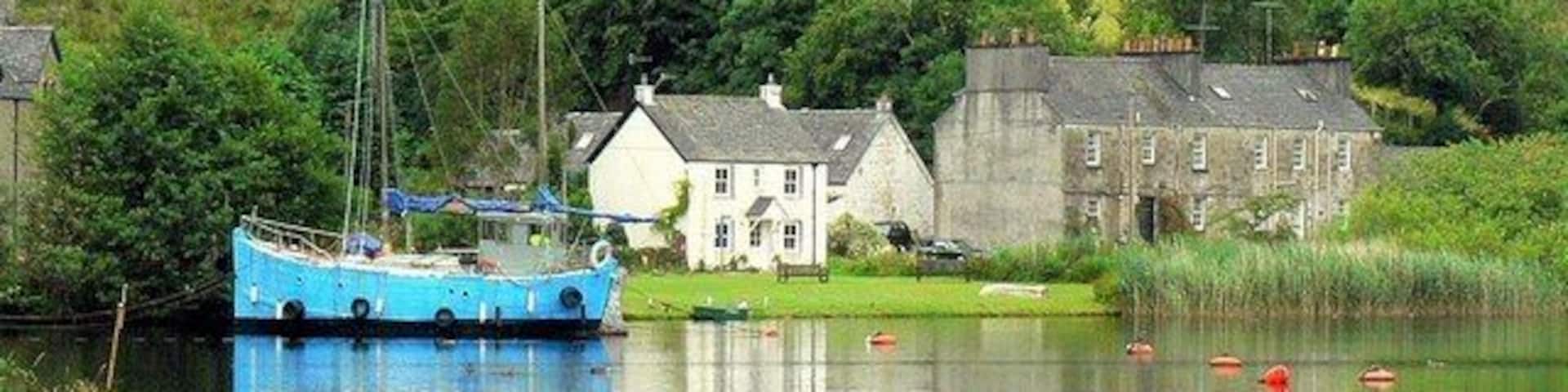 A blue boat docked near a house by a calm lake with reflections of the surroundings.