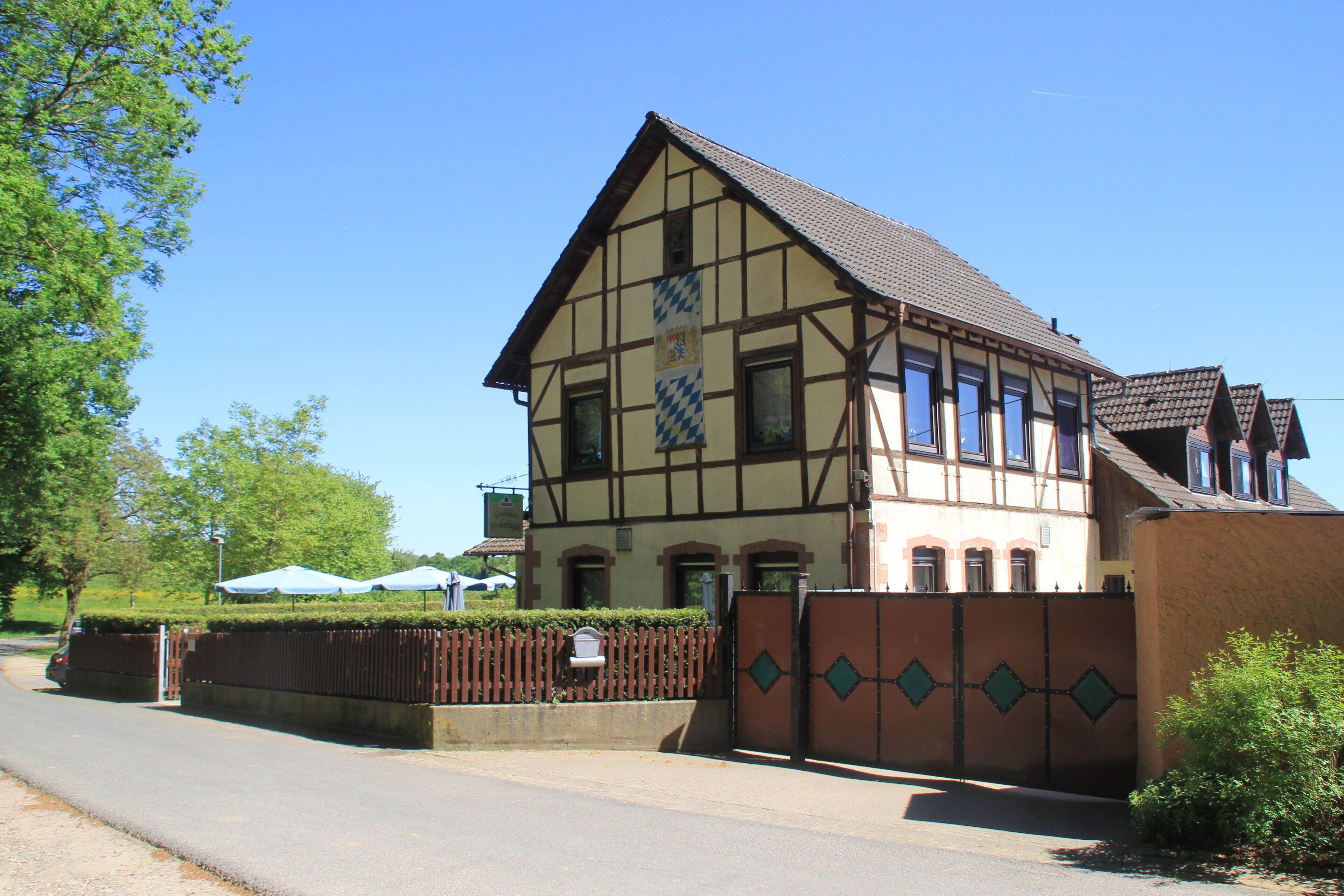 A traditional half-timbered house with a tiled roof, a gated entrance, and a clear blue sky.