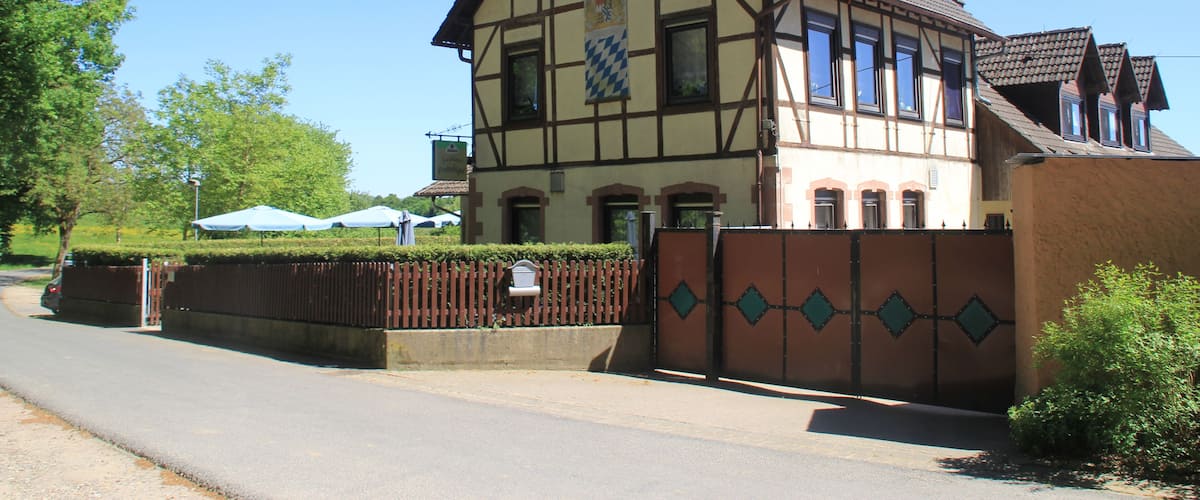 A traditional half-timbered house with a tiled roof, a gated entrance, and a clear blue sky.